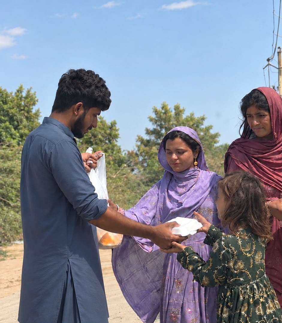 A volunteer handing a meal box to a mother and her daughters